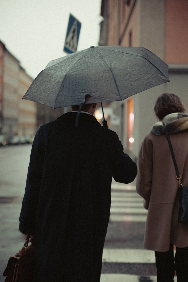 Hampus Wikerstål och Elin Ternert är påväg bort från kameran. Dom går på ett övergångställe och är påväg bort från kameran. Det regnar och Hampus håller i ett paraply.